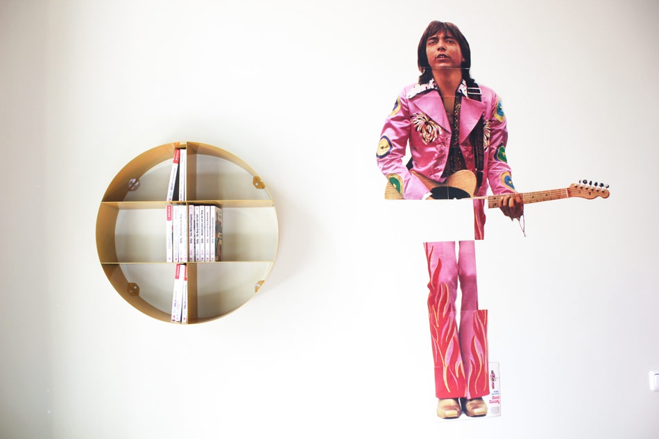 Nahaufnahme einer Wand im Themenzimmer des Postels in Wolgast. Ein kreisrundes Regal und daneben ist ein Musiker mit Gitarre tapeziert.