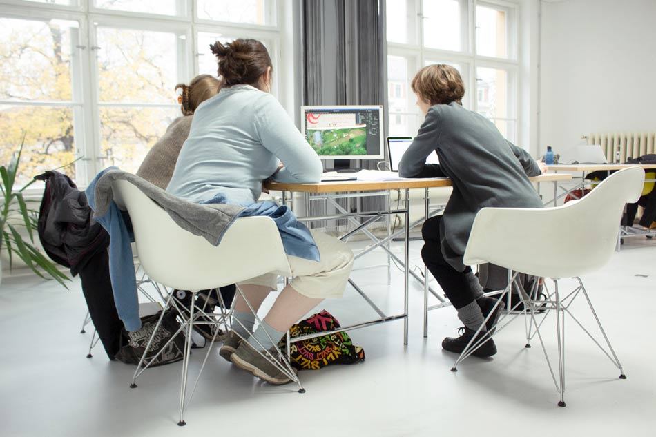 Bild von drei Personen die um einen Computer sitzen und miteinander kommunizieren.