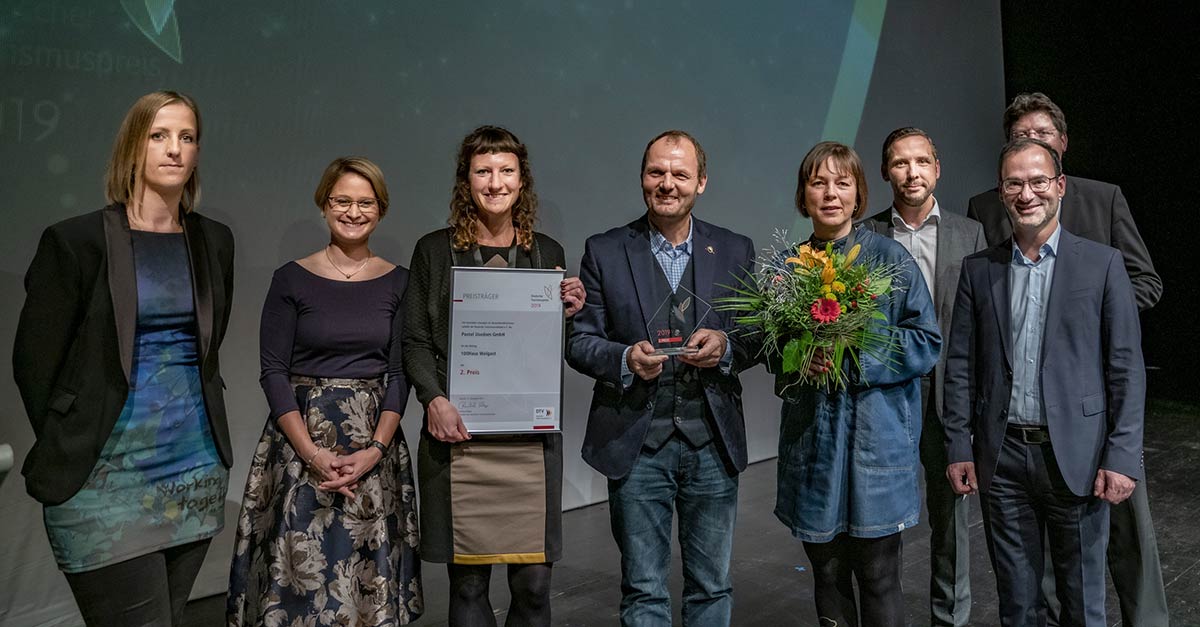 Foto Siegerehrung deutscher Tourismuspreis 2019. Personengruppe auf Bühne, in der Mitte Chefin von Cubus Plan mit Urkunde.