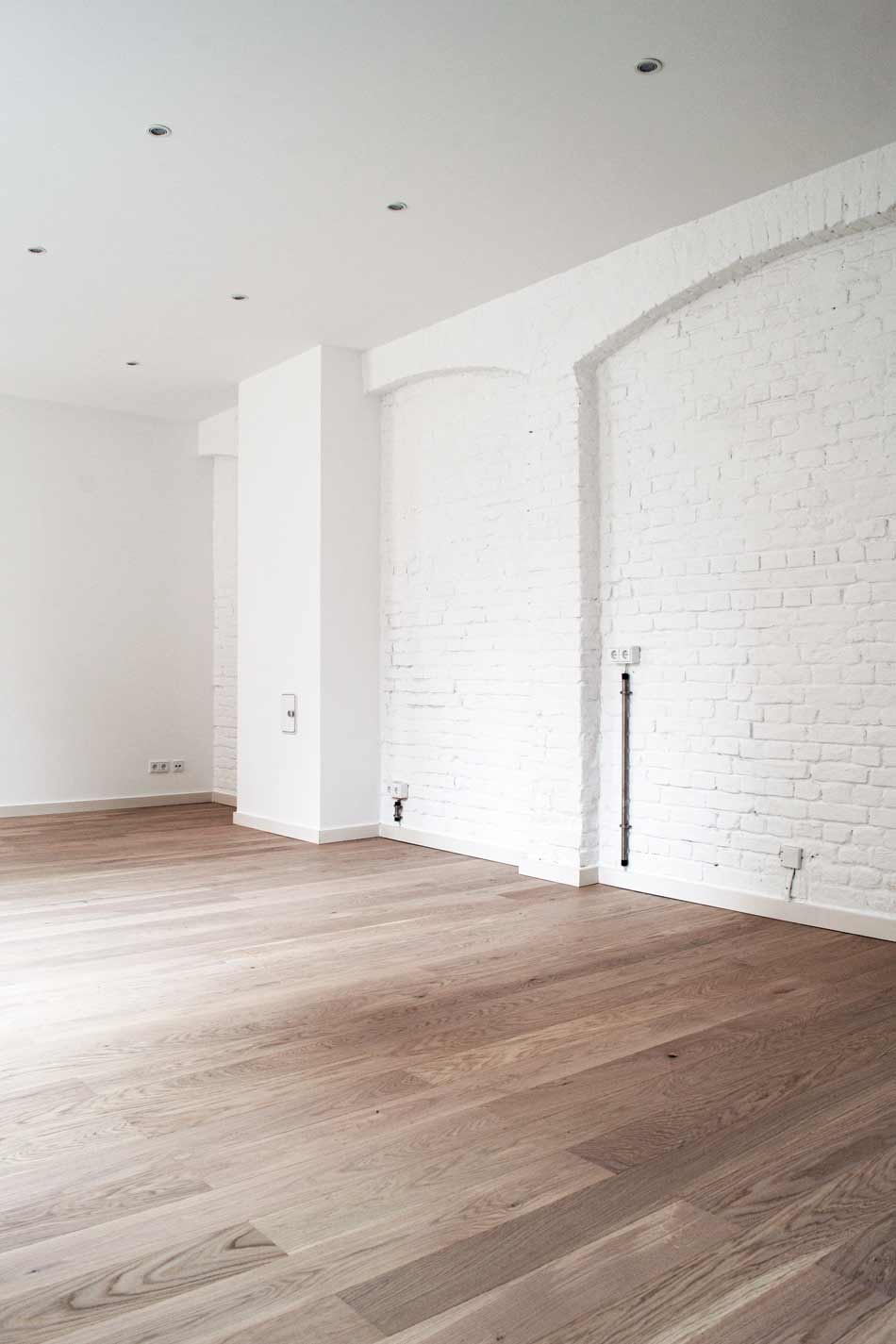 Innenraum der sanierten Remise Schöneweide. Die Wand besteht aus weiß bemalten und geputzten Backsteinen. Der Boden ist aus Holz.
