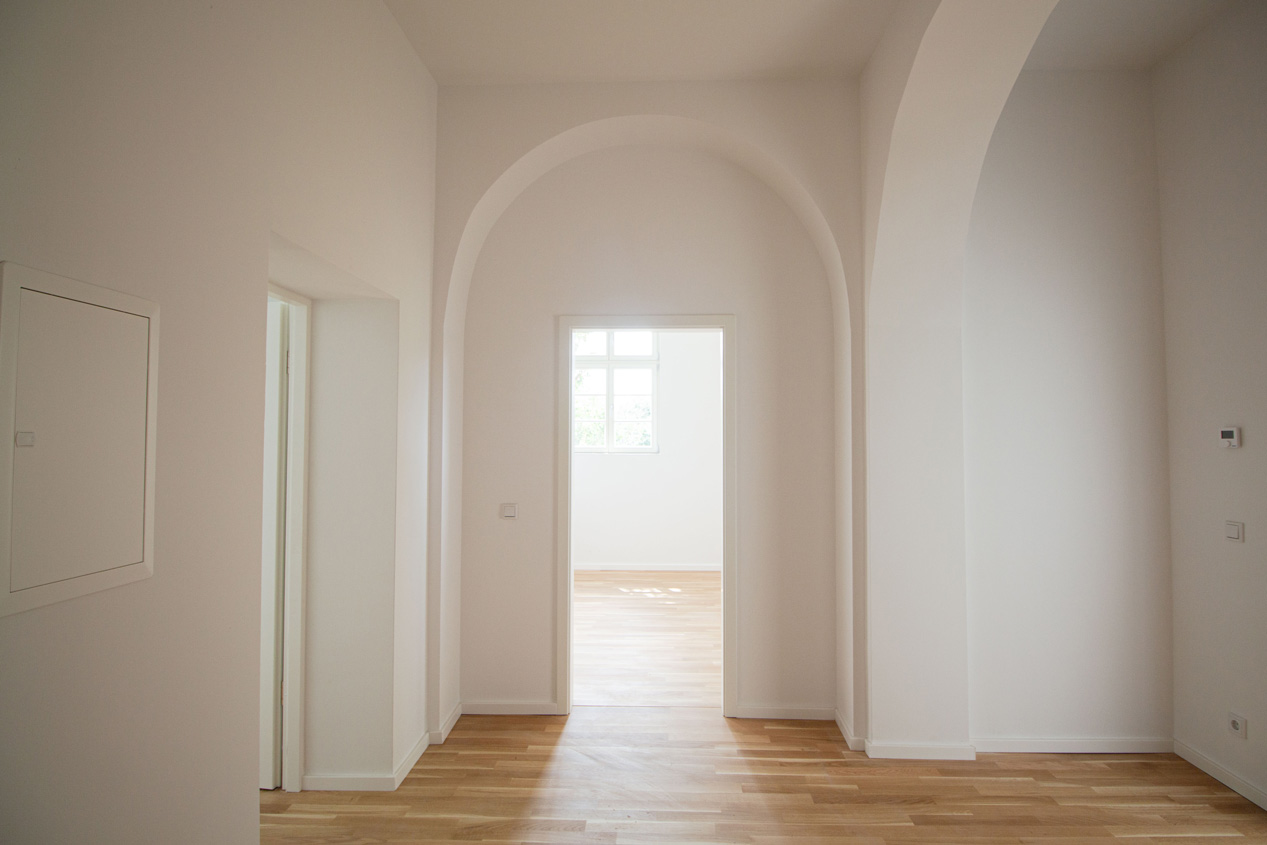 Foto eines Innenraumes des Manschaftsgebäudes INFA. Die Wände des Raumes sind weiß und verfügen Teils über Rundbögen im Oberen Teil.