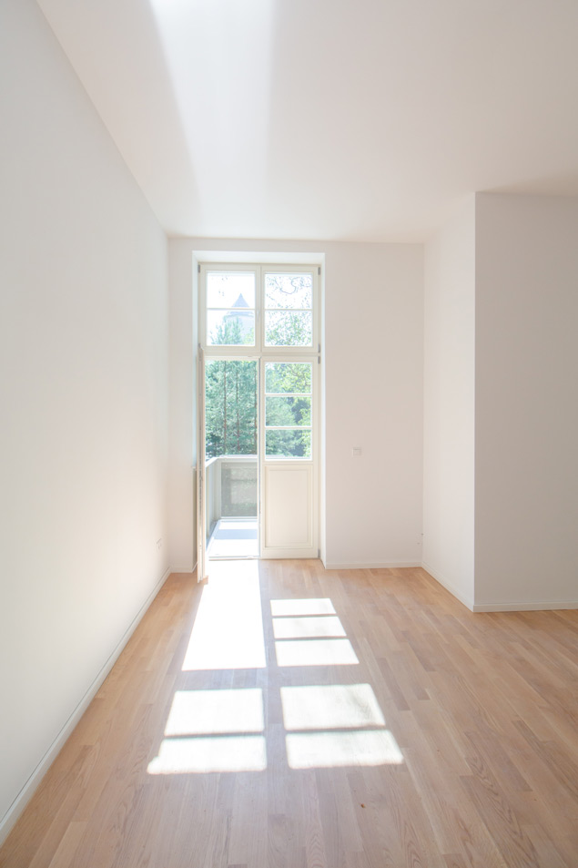 Lichtdurchflutete Innenansicht eines Zimmers des Stabsgebäudes mit Ausblick auf den Balkon und Vegetation vor dem Gebäude.