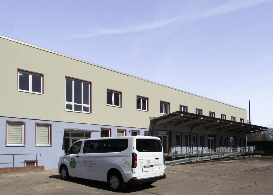 BAHN5-8_cubus-plan Ansicht des EFJ-Wohngebäudes mit zweifarbiger Zonierung, unten sanftes Blaugrau oben helles Grün. Rollstuhlzugang, barrierefreier Eingang des Umbaus mit Vordach.