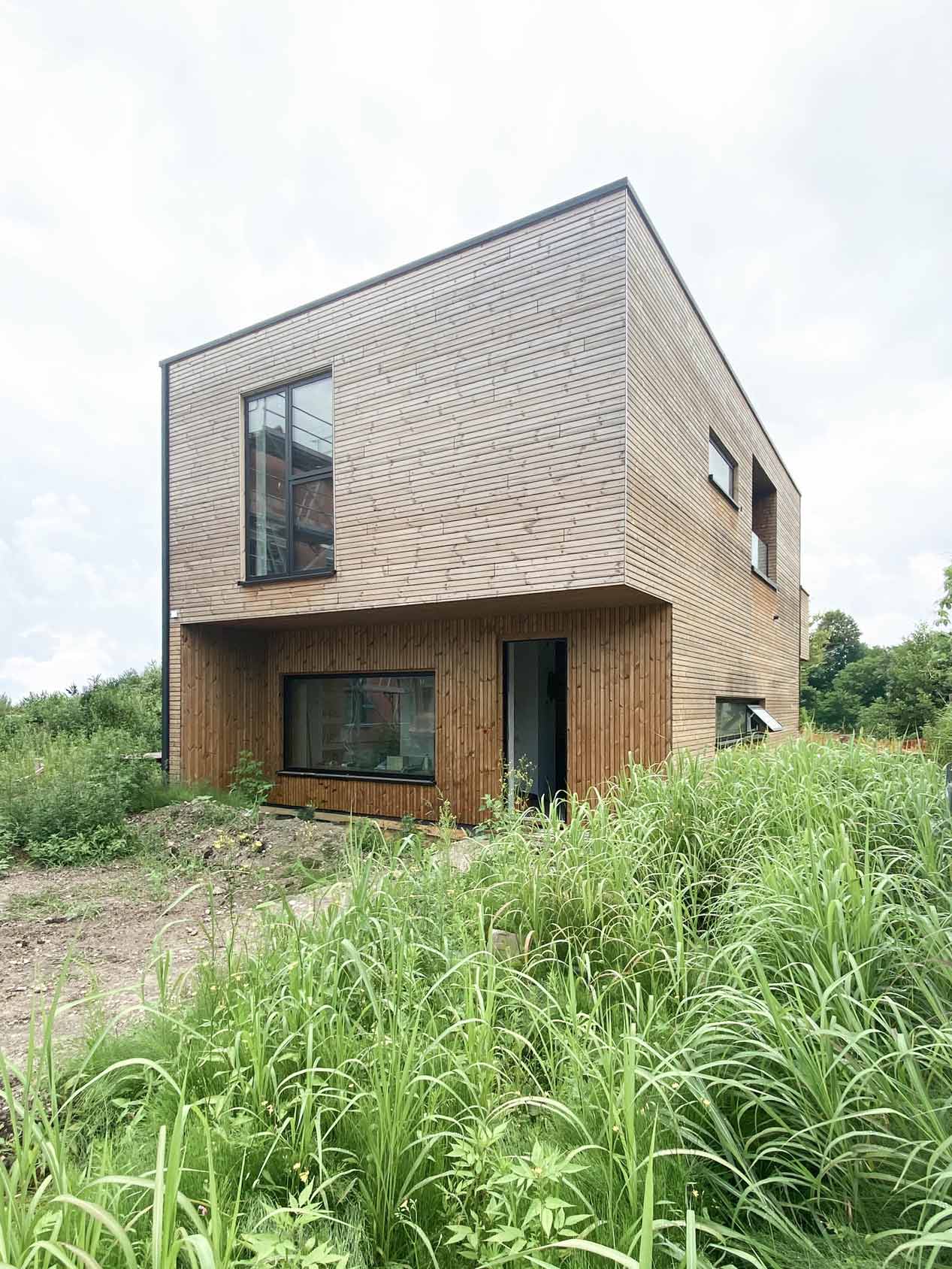 Ansicht des Gebäudes während der Bauarbeiten mit hohem Gras im Vordergund.