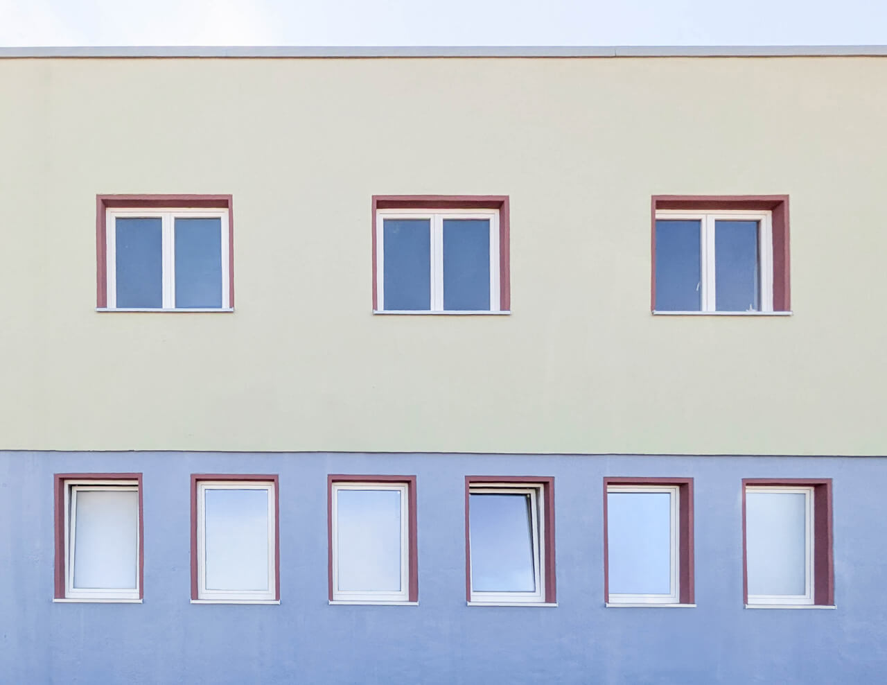 Fassadenansicht des EFJ-Wohngebäudes mit zweifarbiger Zonierung, unten sanftes Blaugrau oben helles Grün. Die Fensterfaschen sind in Bordeauxrot gehalten.