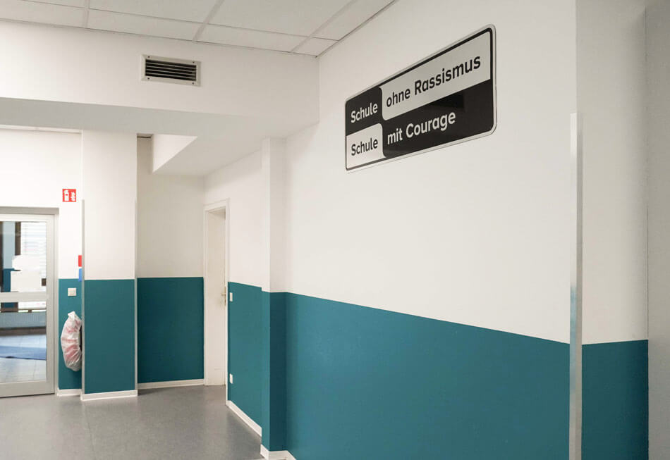 KUEH22-23_cubus-plan Flur in weiß und blau der Quinoa-Schule mit Schild "Schule ohne Rassismus, Schule mit Courage"