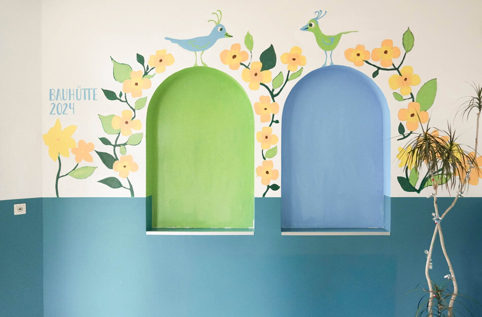 KUEH22-Bauhütte_cubus-plan Wandgestaltung, Wandnischen in grün und blau in der Quinoa-Schule, Bauhütte 2024, gelbe Blüten, zwei Vögel und grüne Blätter aufgemalt.