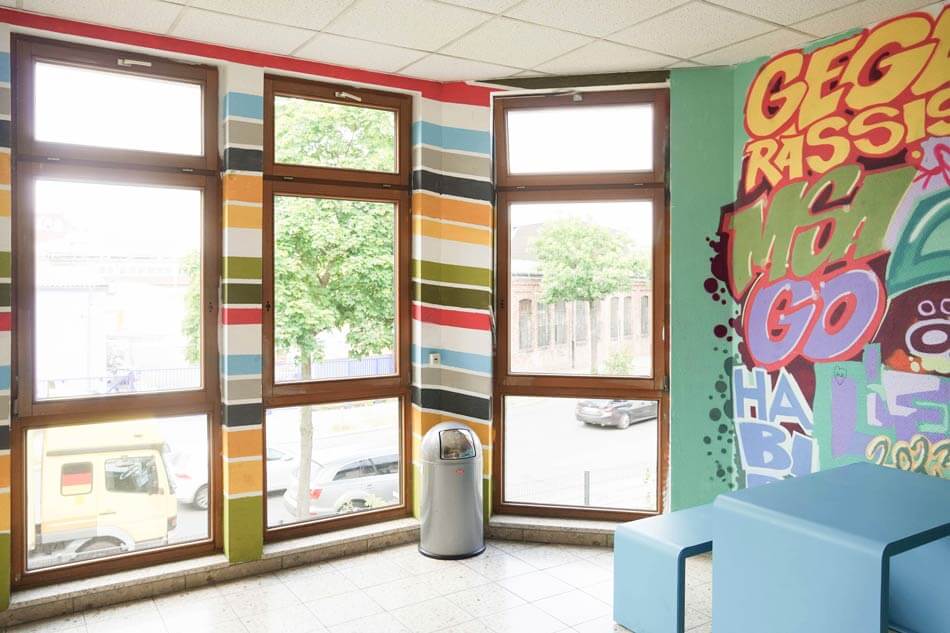 KUEH22-25_cubus-plan Innenraum mit Graffiti an der Wand und Tisch mit Sitzgelegenheit in blau.