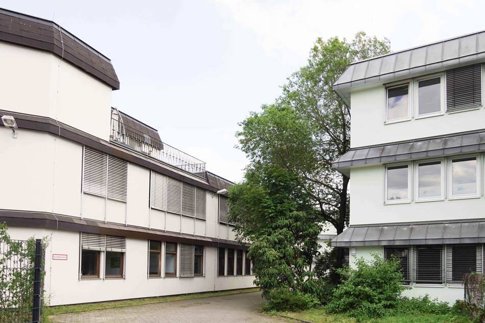 KUEH22-32_cubus-plan Beide Gebäudeteile der Quinoa-Schule mit viel Vegetation dazwischen.