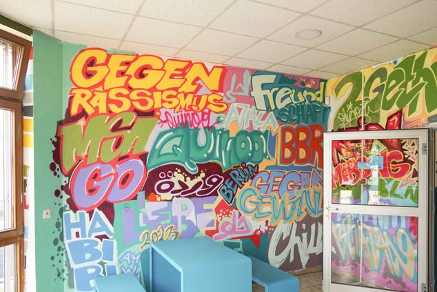 KUEH22-Graffiti_cubus-plan eine Wand mit Graffiti und Tisch und Bänken in blau.