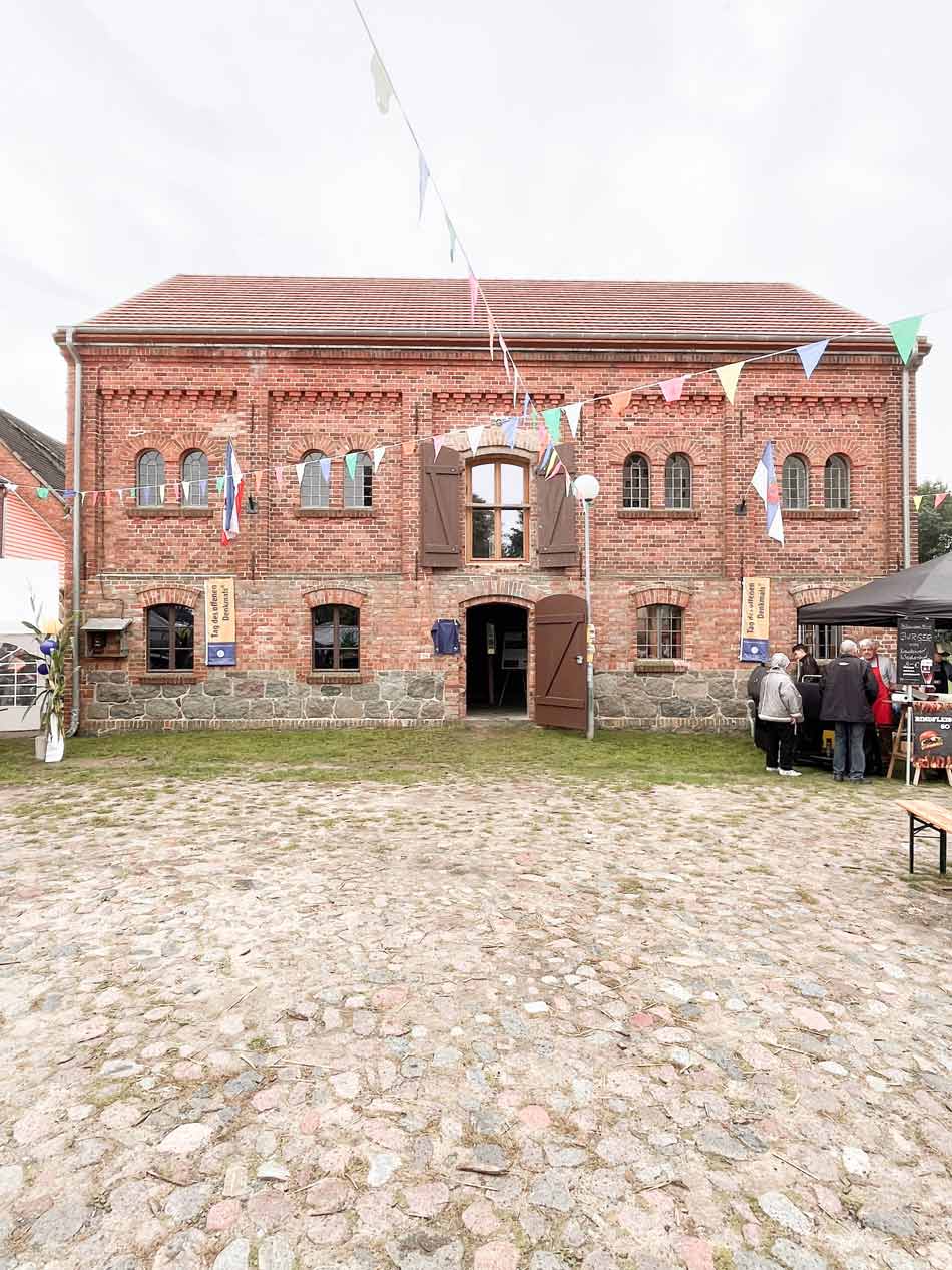 Ansicht des Regionalladens am Schloss Penkun zum Tag des offenen Denkmals im September 2025 mit Wimpelketten und einem Grillstand und Besuchenden.
